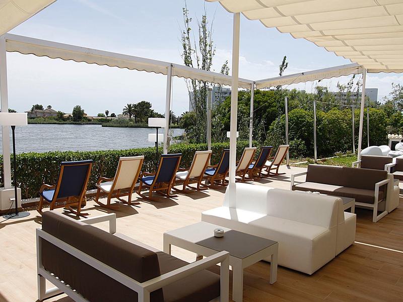 Modernes Outdoor-Lounge mit Sesseln und Liegestühlen am Wasser unter Sonnensegeln.