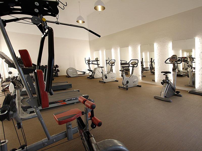 Helles Fitnessstudio mit verschiedenen Trainingsgeräten und durch Fenster beleuchtetem Raum.