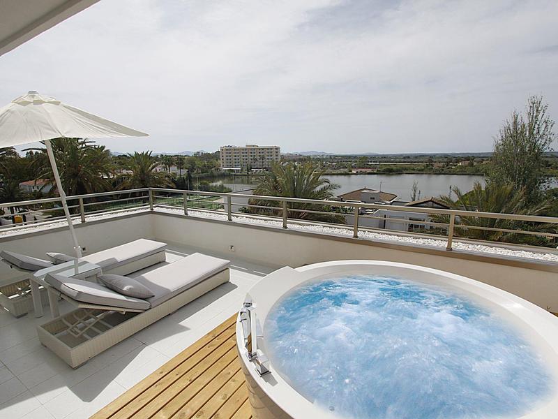 Moderne Terrasse mit Whirlpool, Liegen und Blick auf Wasser und Grünflächen