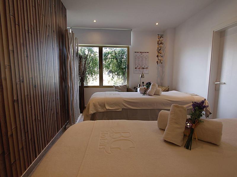 Hell eingerichteter Wellnessraum mit zwei Massageliegen und dekorativen Holzpaneelen an der Wand