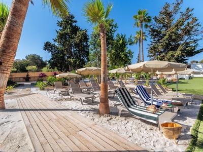 Espace extérieur avec chaises longues, parasols et sable entre des palmiers dans un complexe hôtelier.