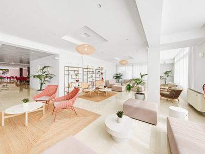 Helles Hotel-Lounge mit rosa Sesseln, weißen Tischen und großer Fensterfront.