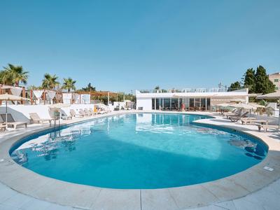 Runder Außenpool mit Liegestühlen und Sonnenschirmen in einem Hotel unter klarem blauem Himmel.