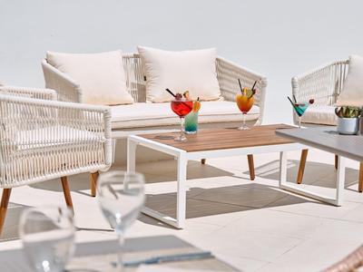 Moderner Sitzbereich mit weißen Sesseln und bunten Cocktails auf einer sonnigen Terrasse.