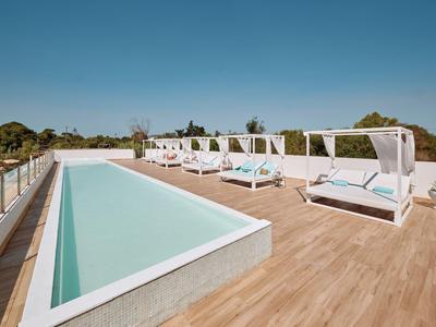 Moderner Poolbereich mit Liegen und Schattenplätzen auf einer offenen Holzterrasse unter blauem Himmel.