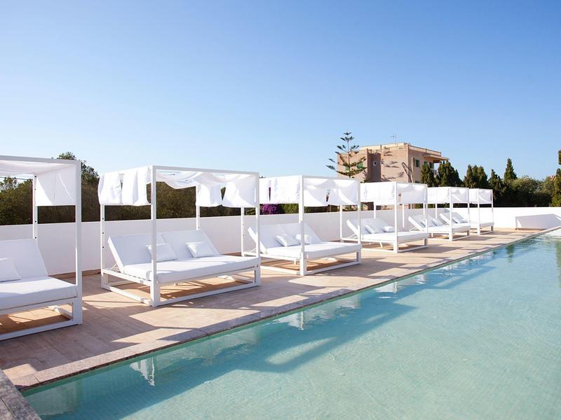 Luxuriöser Poolbereich mit weißen Liegen und Baldachinen unter blauem Himmel.