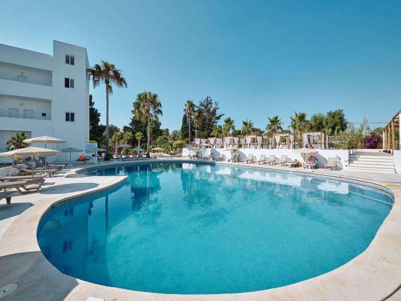 Runder Hotelpool bei Sonnenschein mit Liegestühlen und Palmen im Hintergrund.