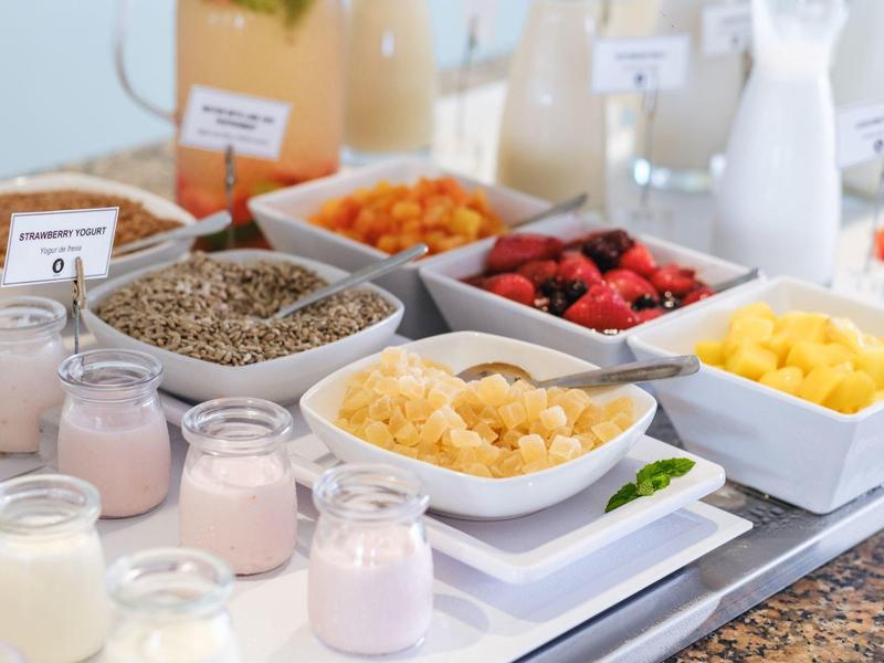 Nahaufnahme eines Frühstücksbuffets mit Müsli, Obst und Joghurt in kleinen Gläsern.