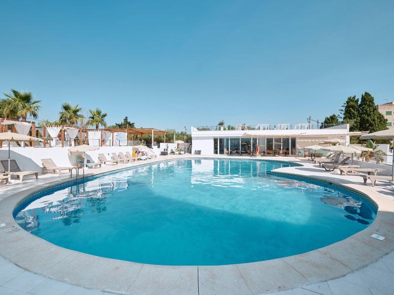 Runder Außenpool mit Liegestühlen und Sonnenschirmen in einem Hotel unter klarem blauem Himmel.