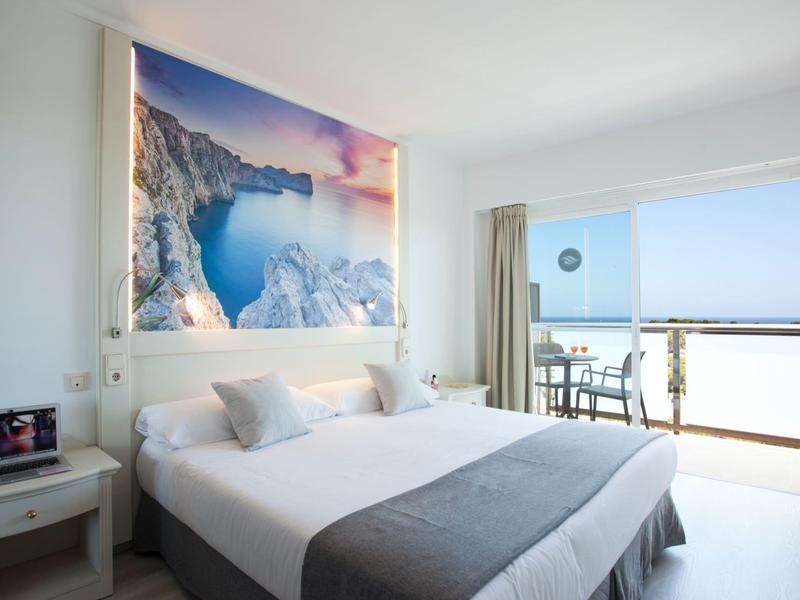 Modernes Hotelzimmer mit Doppelbett, großem Wandbild und Balkon mit Meerblick.