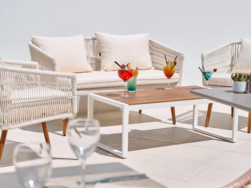 Moderner Sitzbereich mit weißen Sesseln und bunten Cocktails auf einer sonnigen Terrasse.