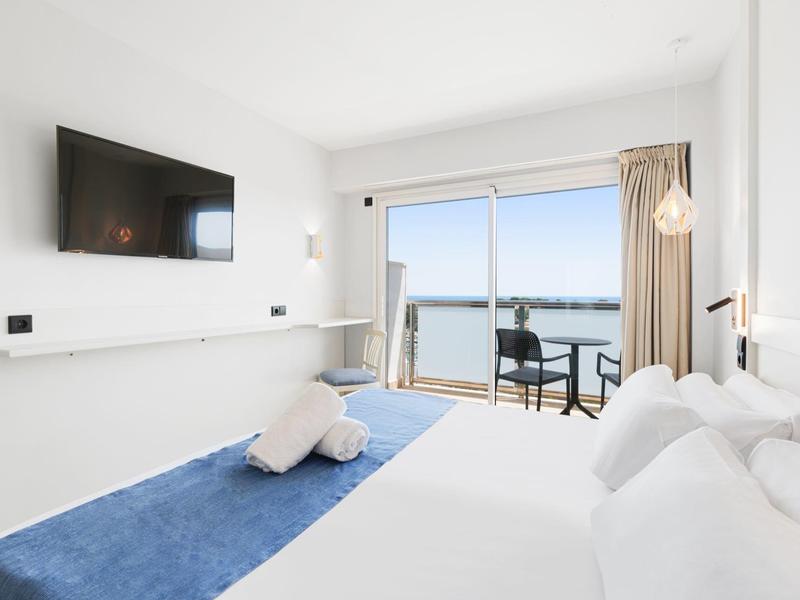 Hell eingerichtetes Hotelzimmer mit Meerblick und Balkon, modernen Möbeln und Flachbildfernseher.