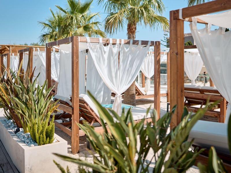 Gemütliche Außenlounge mit weißen Vorhängen und Palmen an sonnigem Tag