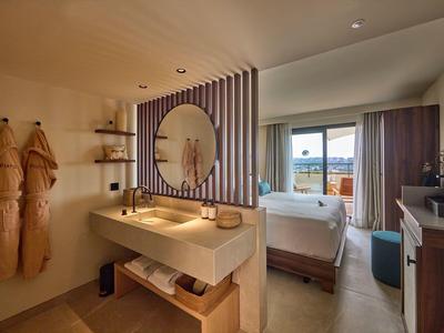 Modernes Hotelzimmer mit Doppelbett, Holzwaschbecken, zwei Bademänteln und Balkon mit Bergblick.