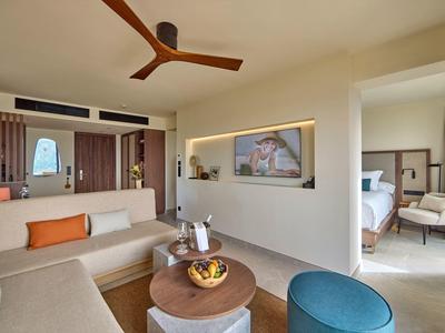 Moderner Wohnbereich mit hellen Wänden, Sofa, Deckenventilator und Zugang zum Schlafzimmer.