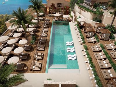 Luxuriöser Außenpool mit Liegestühlen, Sonnenschirmen und Palmen neben klarem Wasser und Meerblick.