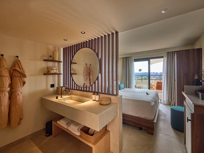 Modernes Hotelzimmer mit Doppelbett, Holzwaschbecken, zwei Bademänteln und Balkon mit Bergblick.