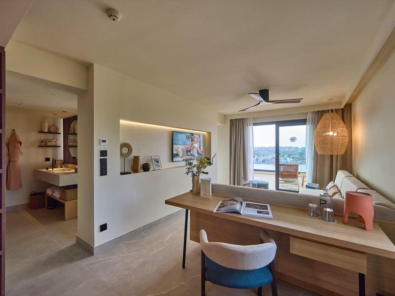 Modern eingerichtetes Wohnzimmer mit Schreibtisch, Stuhl, Sofa, Fenster und warmem Licht.