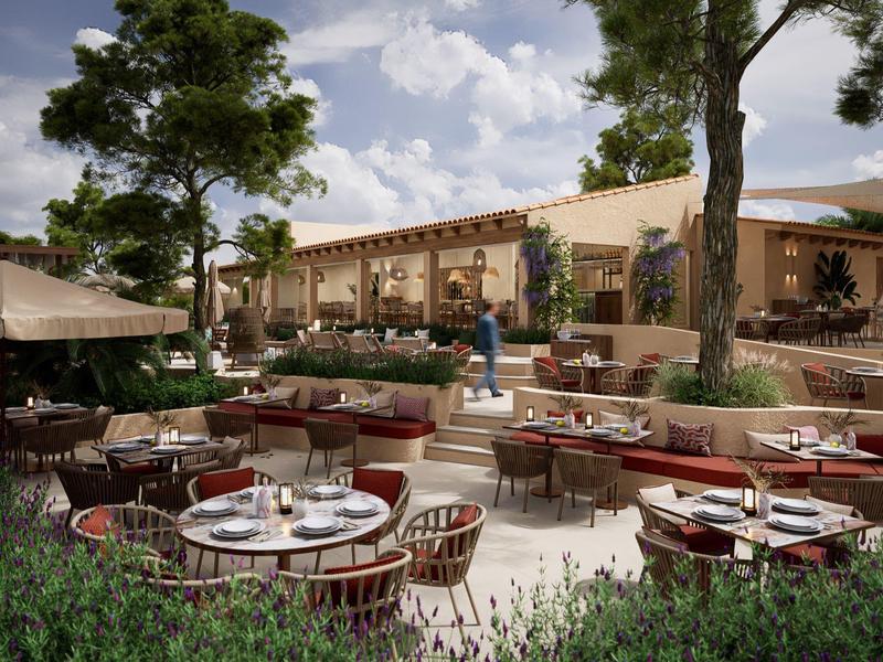 Große Terrasse mit Tischen und Stühlen, umgeben von Bäumen und Pflanzen, darunter Gäste und Bedienung.