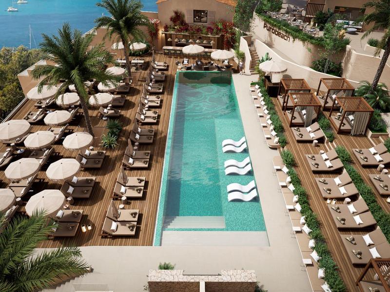 Luxuriöser Außenpool mit Liegestühlen, Sonnenschirmen und Palmen neben klarem Wasser und Meerblick.