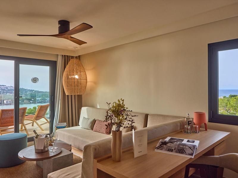 Helles Wohnzimmer mit Sofa, Holztisch, Deckenventilator und Terrasse mit Meerblick.