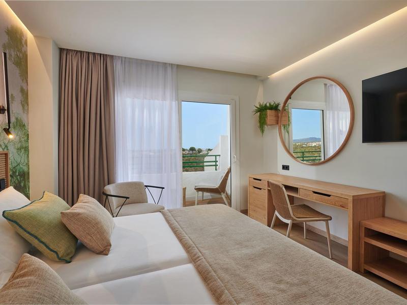 Habitación de hotel moderna con cama doble, escritorio, espejo redondo y balcón con vista al mar.