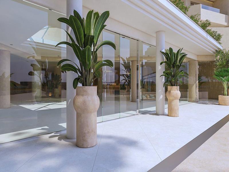 Lobby moderna de hotel con grandes ventanales y plantas decorativas en macetas sobre suelo blanco.