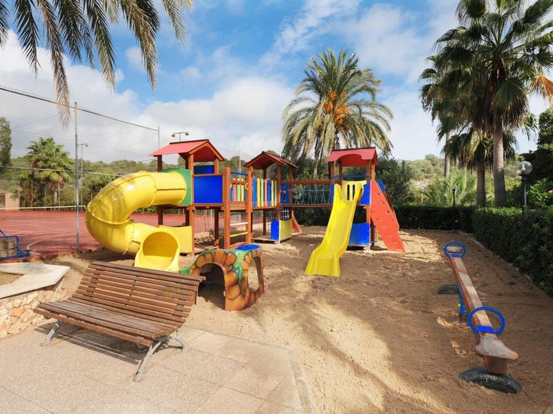 Área de juegos colorida con toboganes y balancín en un jardín de hotel bajo palmeras.