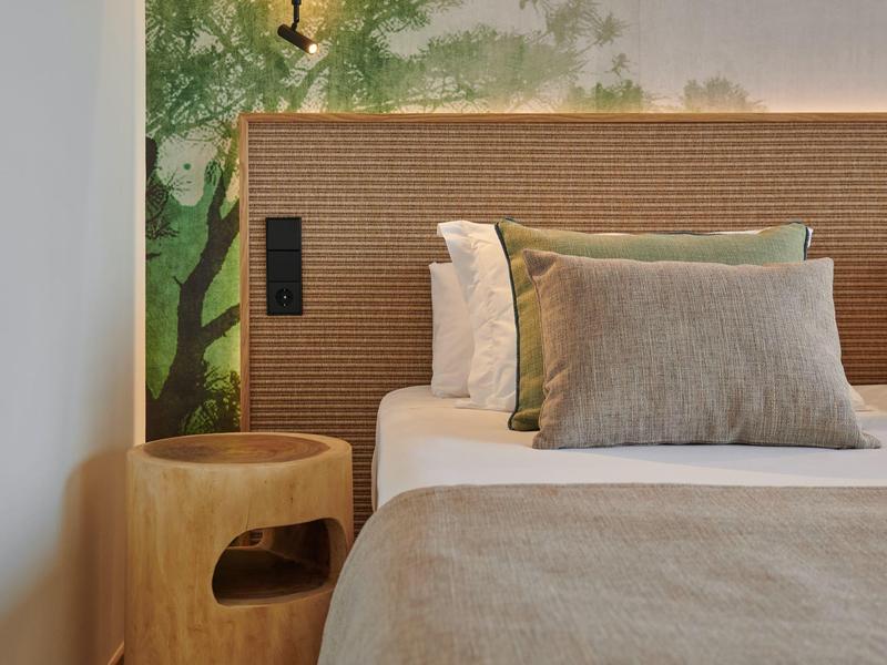 Dormitorio iluminado con cama de madera y motivo natural verde en la pared.