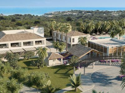 Luchtfoto van een resort met gebouwen, palmbomen, een zwembad en groen landschap bij de zee.