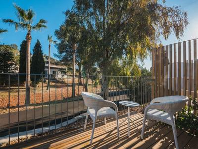 Buiten terras met twee witte stoelen en een klein tafeltje bij bomen en een heldere lucht.