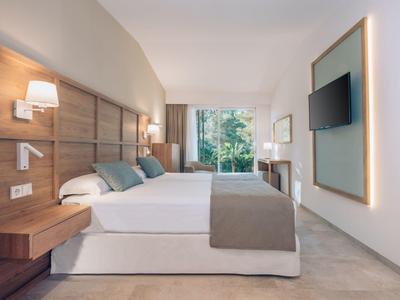 Moderne hotelkamer met tweepersoonsbed, houten hoofdeinde, wandlampen en groot raam met tuinzicht.