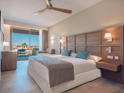 Moderne hotelkamer met twee grote bedden, houten hoofdeinden, zachte verlichting en schuifdeuren naar balkon.