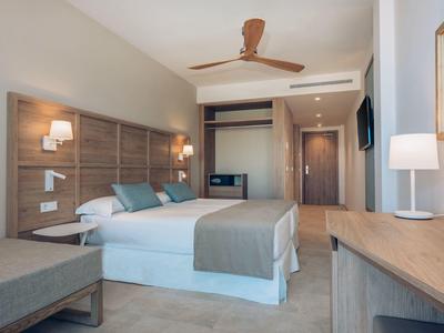 Moderne hotelkamer met een tweepersoonsbed, houten meubels, plafondventilator en neutrale kleuren.