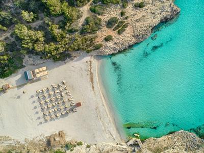 Luchtfoto van een zandstrand met parasols naast helder turquoise water en rotsachtige kliffen.