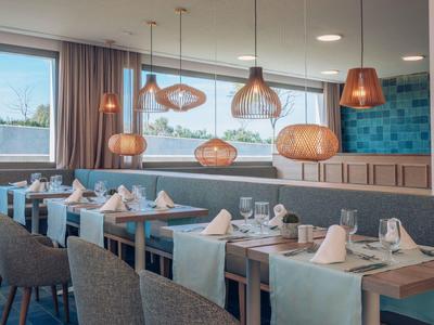 Modern restaurantinterieur met houten tafels, grijze stoelen en hanglampen.