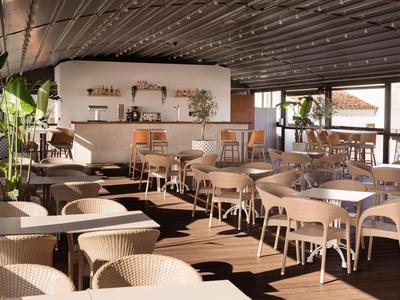 Modern breakfast room with sunlit windows, wooden ceiling, and light-colored chairs.