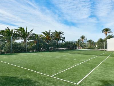 Green tennis court with palm trees and blue sky at a hotel resort.