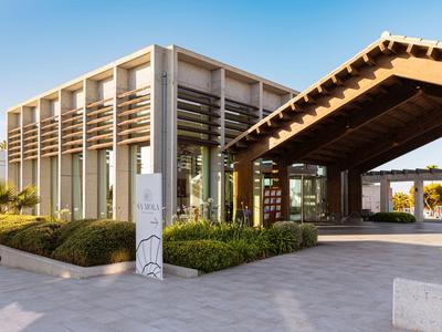 Modern hotel building with large glass facade and covered entrance area under blue sky.