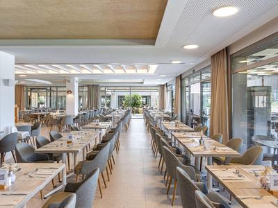 Modern hotel dining area with long tables, chairs, and large windows.