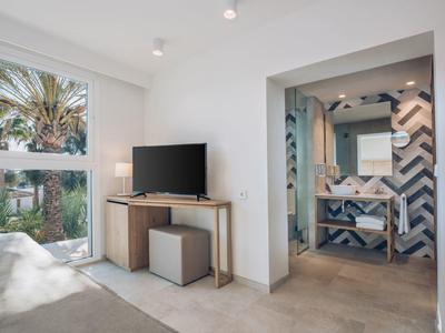 Lichte hotelkamer met tv, houten console, badkamer met patroon tegels en groot raam.