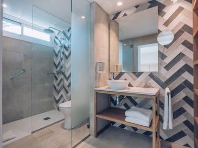 Moderne badkamer met glazen douche, houten wastafelmeubel, patroonwand en grote spiegel.