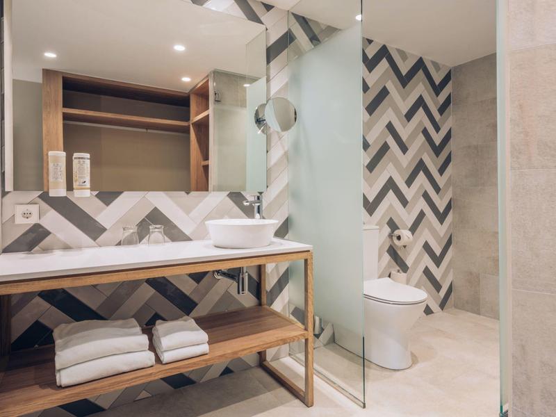 Moderne badkamer met houten wastafelmeubel, witte wasbak, visgraat tegelwand en glazen douchedeur.