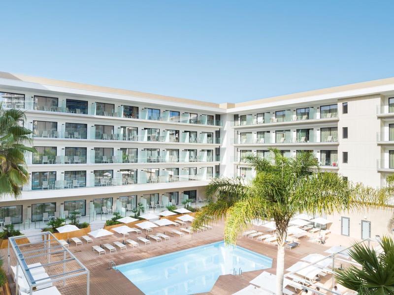 Piscina de hotel moderna con tumbonas y palmeras, rodeada de un edificio blanco con balcones.