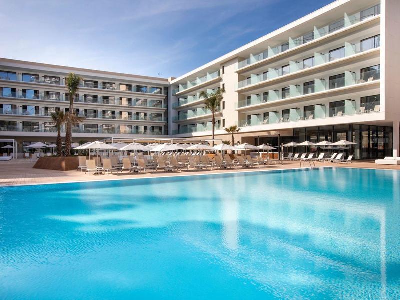 Complejo hotelero moderno con gran piscina exterior y tumbonas bajo cielo despejado.