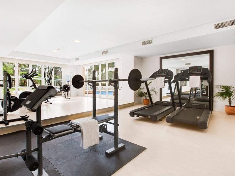Gimnasio moderno con banco de pesas, cintas de correr y grandes ventanas con vista al verde.