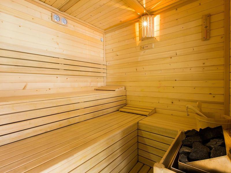 Interior de una sauna de madera con bancos y estufa con piedras.