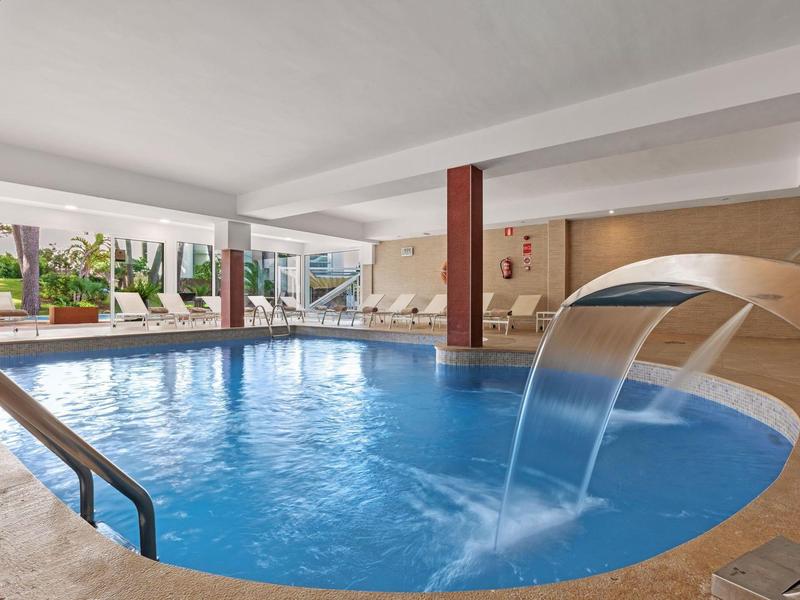 Piscina cubierta con cascada y paredes de vidrio que dan a un área exterior con tumbonas.