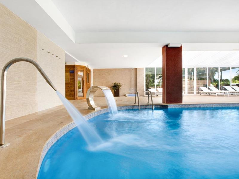 Piscina interior moderna con cascadas y grandes ventanales en un hotel.