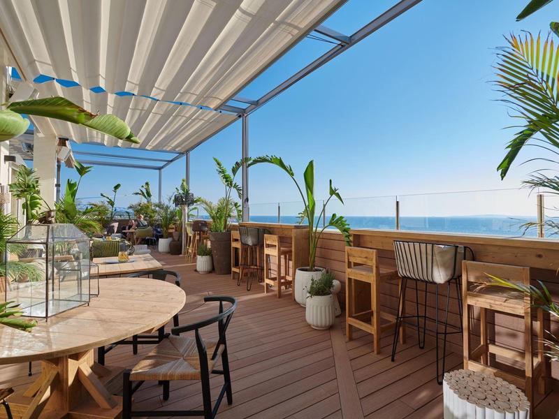 Terraza abierta con muebles de madera y vista al mar bajo cielo despejado.